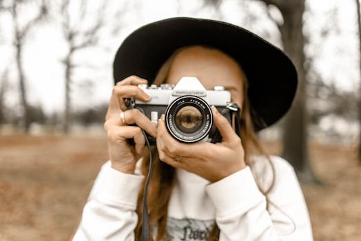 pexels-photo-1051076-1051076-1 Stylish woman in black hat holding a vintage camera outdoors during fall.