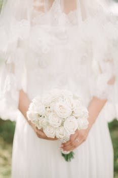 Closeup of a bride in an elegant lace gown holding a white rose bouquet.